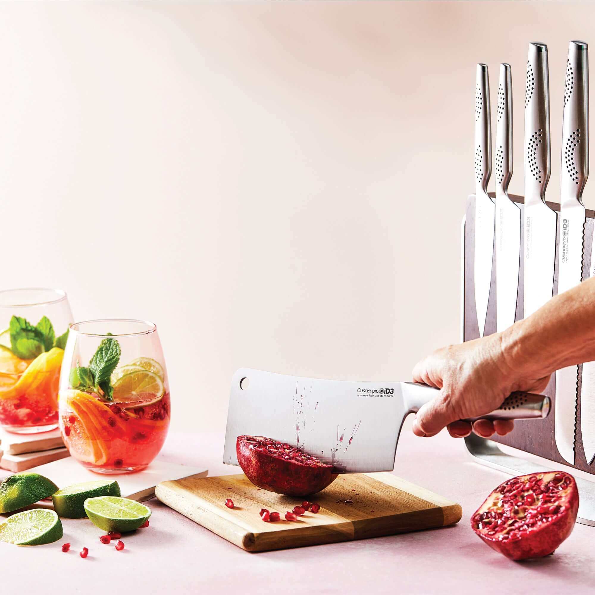 Slicing pomegranate with Cuisine::pro® iD3® Nakano knife set on a wooden board, stylish knife block, fresh drinks and lime wedges in the background