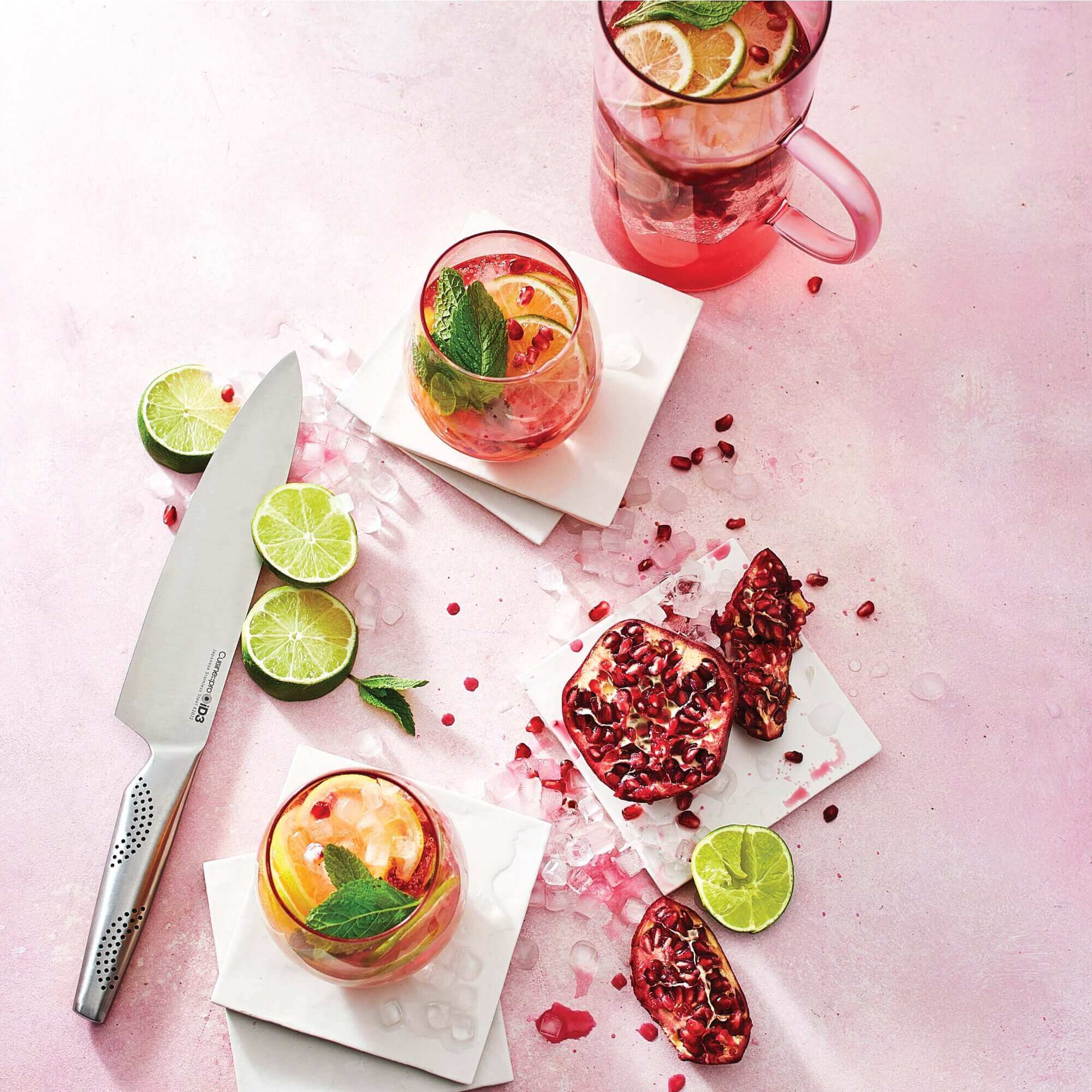 Cuisine::pro® iD3® Nakano knife with sliced limes, pomegranate, and refreshing drinks on a pink background