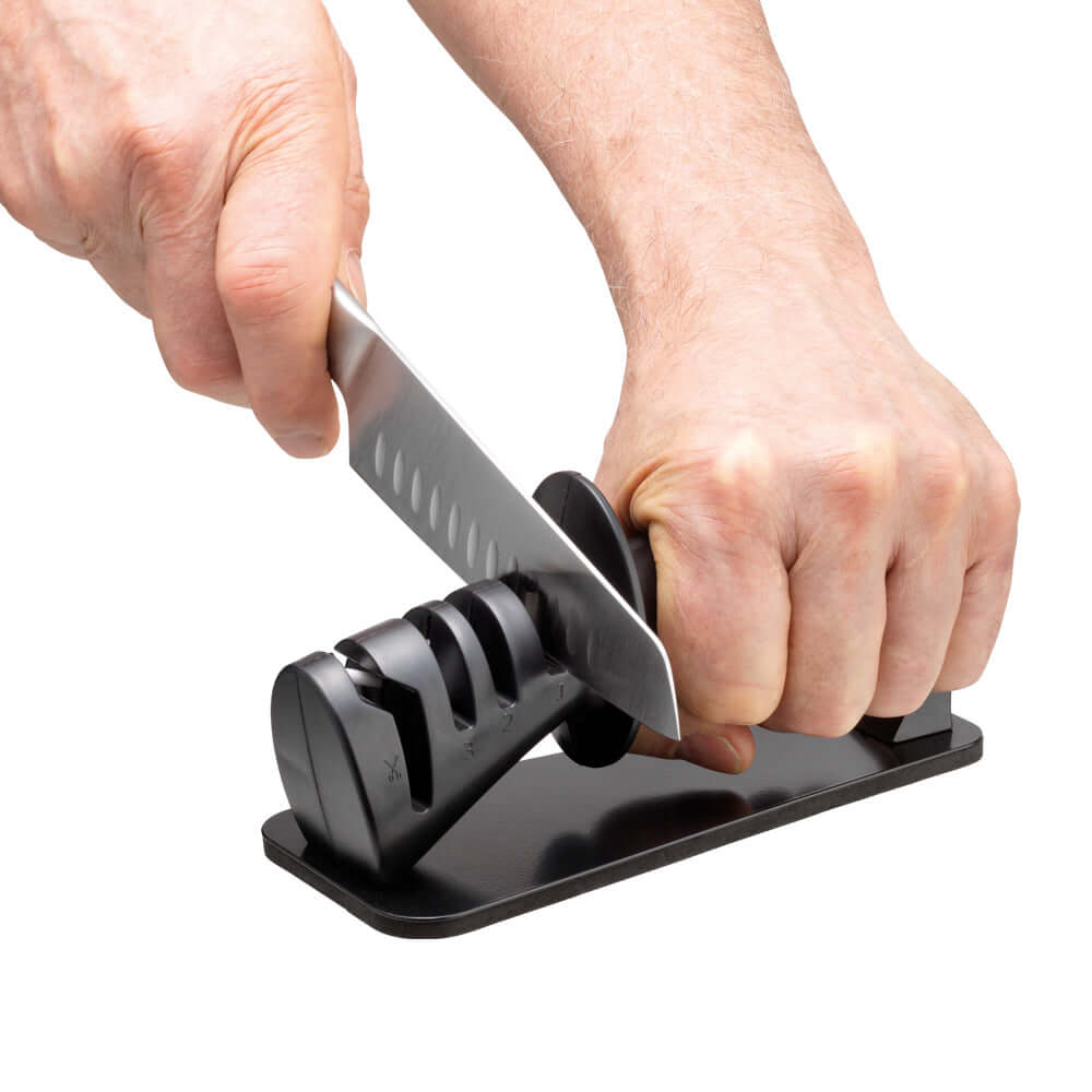 Hands sharpening a Japanese knife with the Cuisine::pro® iD3® BLACK SAMURAI™ 3-Step Knife Sharpener using diamond and ceramic wheels.